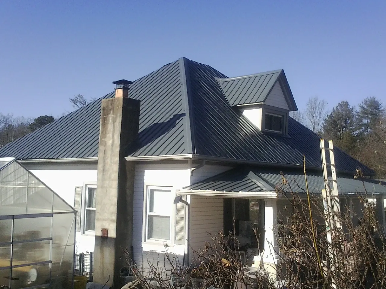 Dark blue standing seam metal roof on a white farmhouse with dormer — Slate & Tile Roof Repair by Roofing Brothers in Long Valley