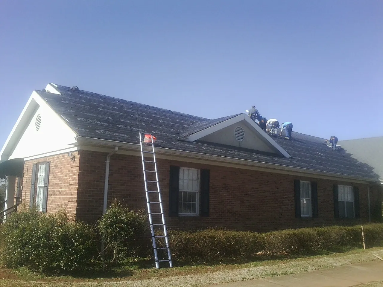 Crew tearing shingles off a brick ranch roof with a ladder set — Metal Roof Repair work by our crew in Long Valley