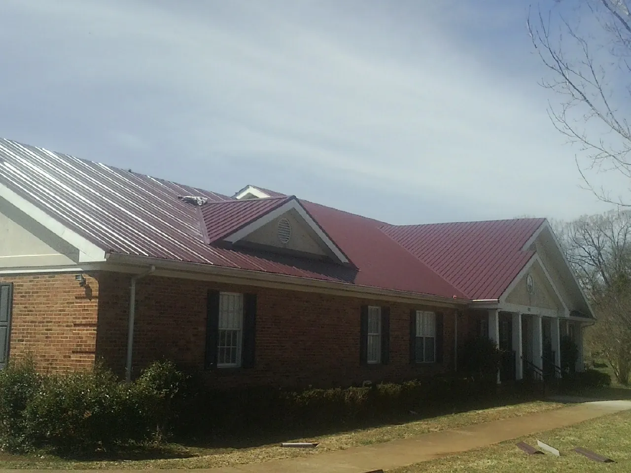 Red metal roof with gabled entries on a long brick building, from a Hail Damage Roof Repair job in Long Valley