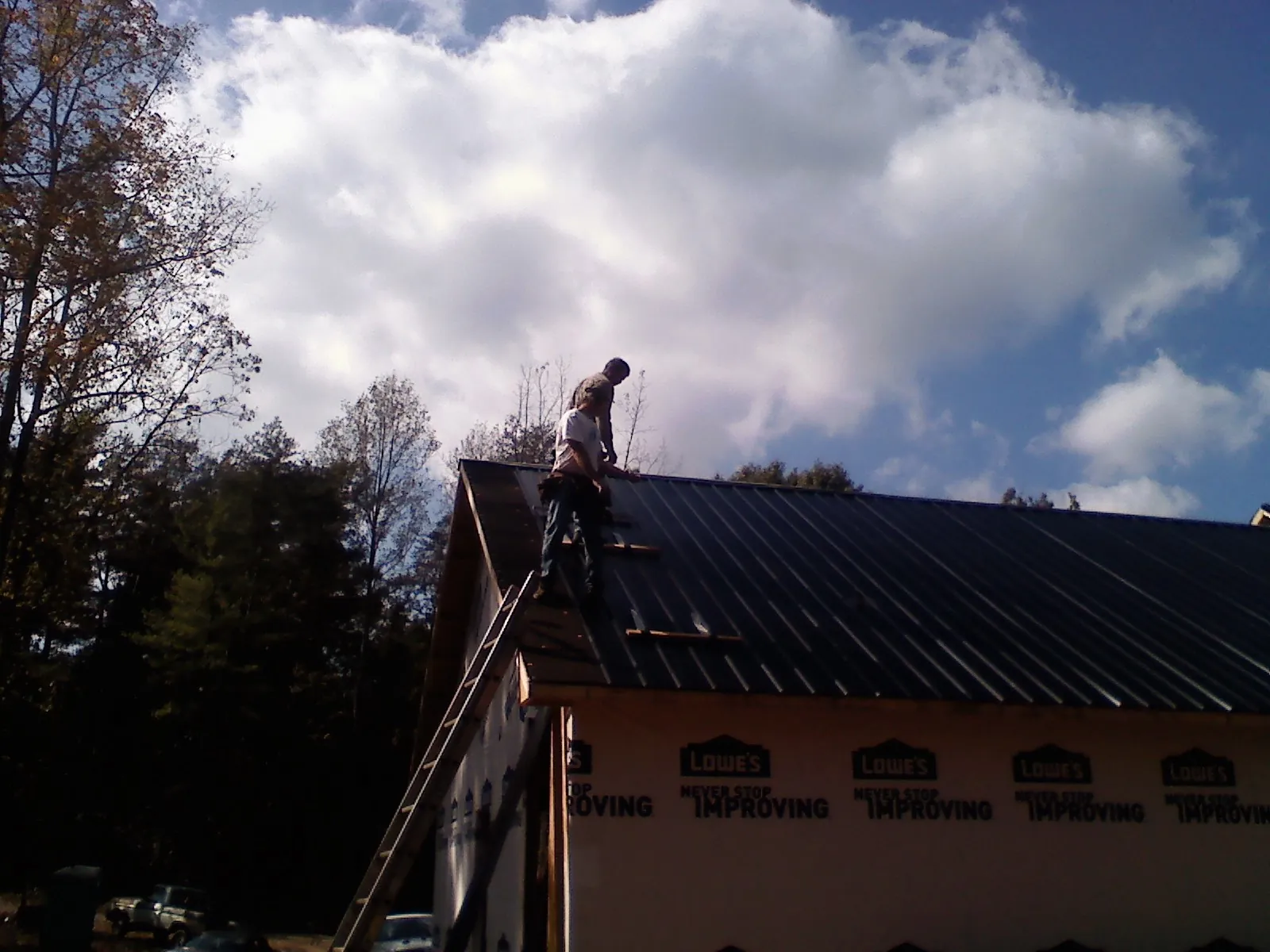 Roofer fastening dark metal panels high against a cloudy sky, from a Roof Inspection job in Long Valley