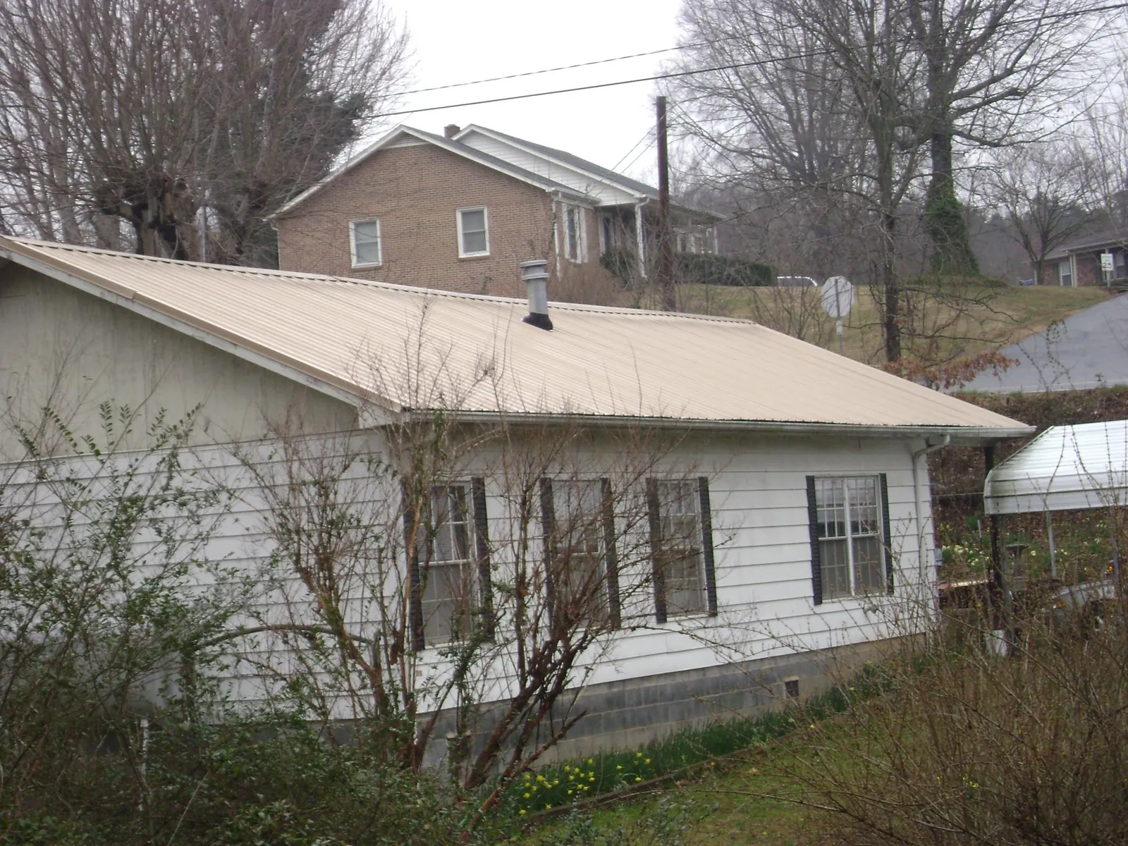 Tan metal roof on a white sided house set into a hillside — Commercial Roofing by Roofing Brothers in Long Valley